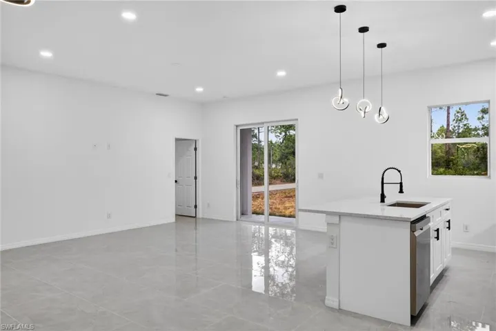 Kitchen with light stone counters, an island with sink, white cabinetry, pendant lighting, and stainless steel dishwasher