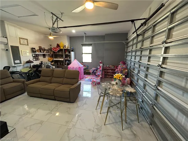 Living room with a garage, electric panel, light marble finish floors, and ceiling fan