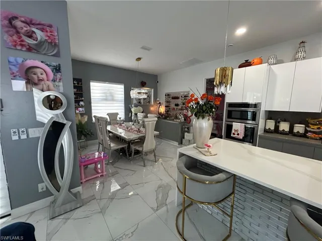 Kitchen with white cabinetry, light stone countertops, hanging light fixtures, and stainless steel double oven