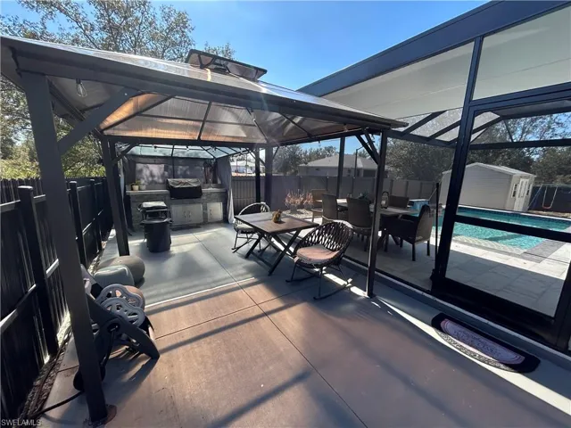 Fenced backyard with a shed, a patio, glass enclosure, a gazebo, and an outdoor kitchen / dining area