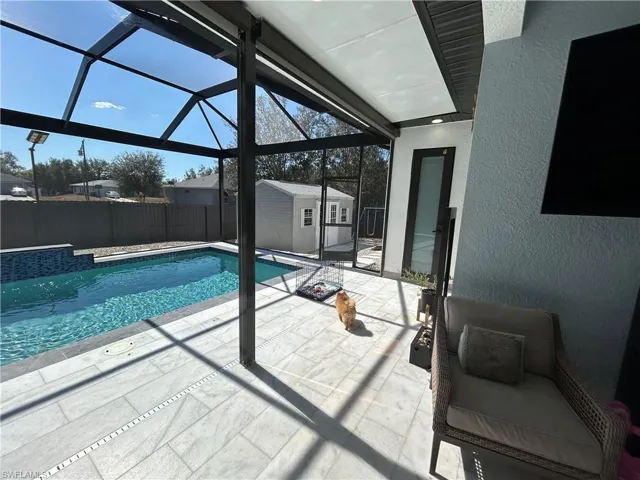 View of pool featuring patio surround, glass enclosure, a sunroom, and a storage unit