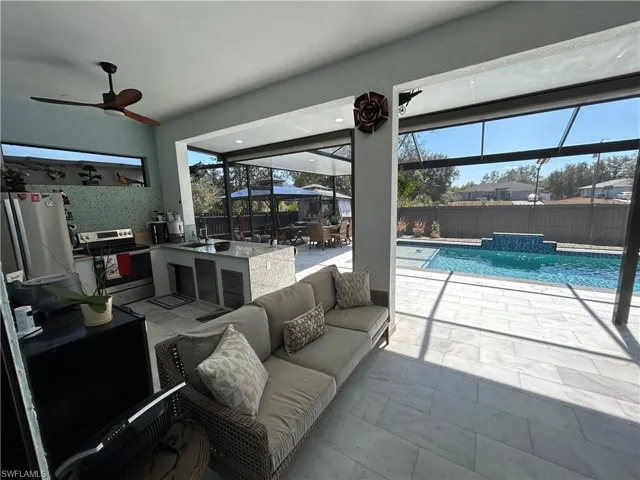 Fenced backyard with a lanai, a patio, an outdoor kitchen with living area, ceiling fan, and a sunroom