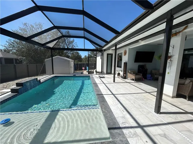 View of pool with patio surround, a fenced backyard, a storage unit, and a sunroom