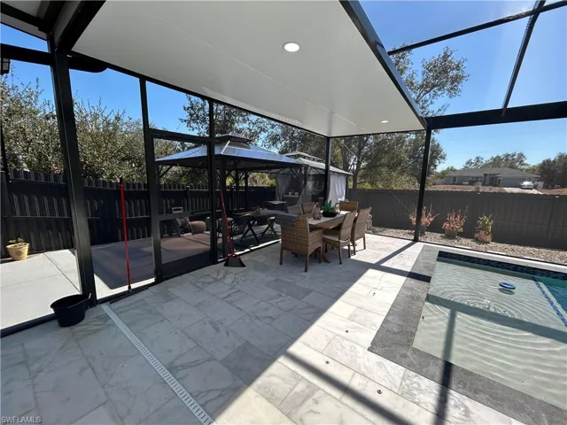 Fenced backyard featuring glass enclosure, outdoor dining area, an outdoor pool, a patio, and a gazebo