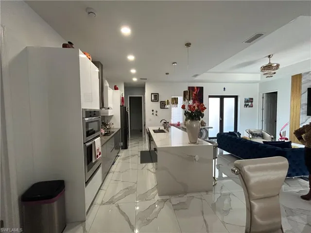 Kitchen featuring decorative light fixtures, french doors, modern cabinets, an island with sink, and white cabinets