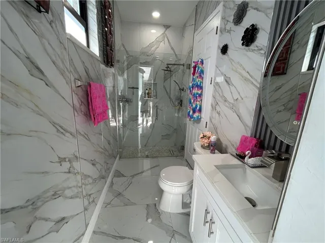 Full bathroom featuring vanity, a marble finish shower, stone wall, and recessed lighting
