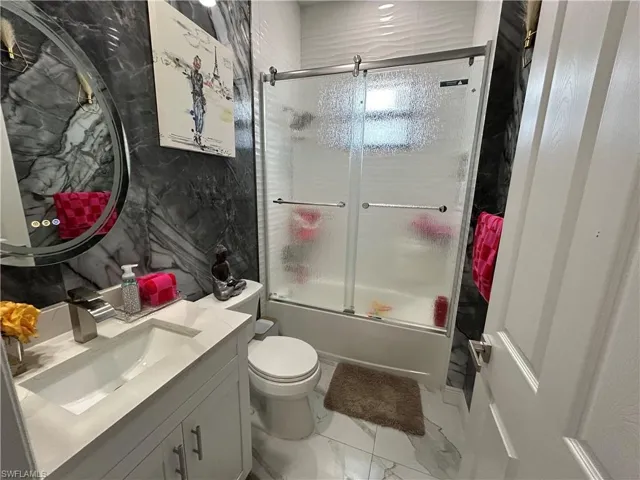 Bathroom featuring enclosed tub / shower combo, vanity, and light marble finish floors