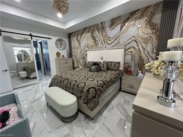 Bedroom with an accent wall, light marble finish flooring, a barn door, recessed lighting, and ensuite bathroom