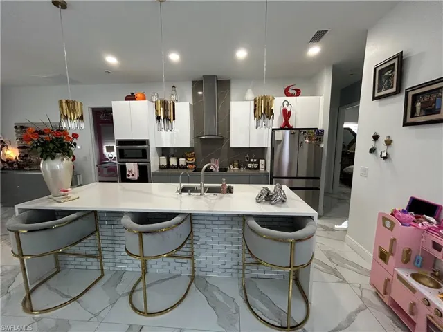 Kitchen with a center island with sink, modern cabinets, white cabinetry, stainless steel appliances, and a kitchen bar