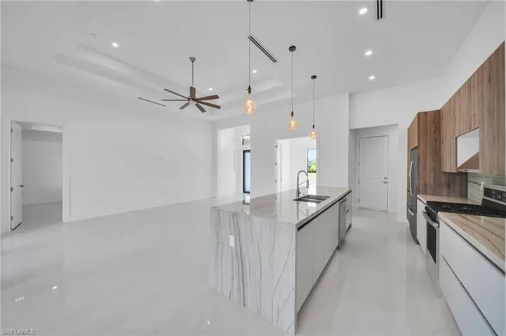 Kitchen with modern cabinets, appliances with stainless steel finishes, a tray ceiling, a large island with sink, and brown cabinets