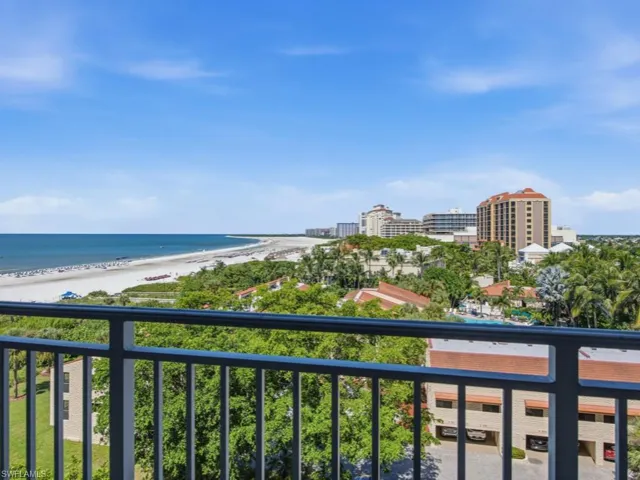 Private balcony with metal railing overlooking the coastline, sandy beach, and surrounding vegetation