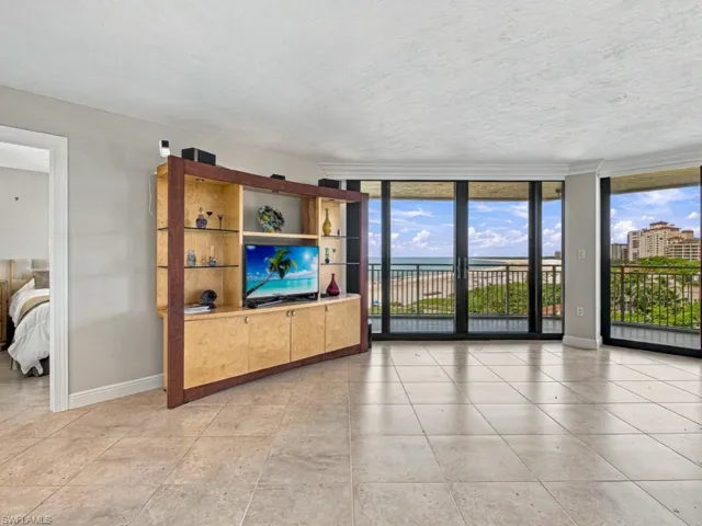 Living space featuring stone tile flooring, built-in light-wood cabinetry, crown molding, floor-to-ceiling windows, and access to a balcony with ocean scenery
