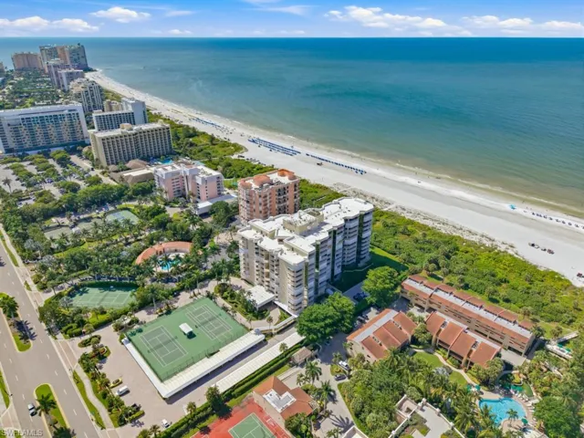 Aerial perspective of beachfront property featuring direct shoreline access, multiple hard-surface tennis courts, outdoor swimming pools, and manicured tropical landscaping