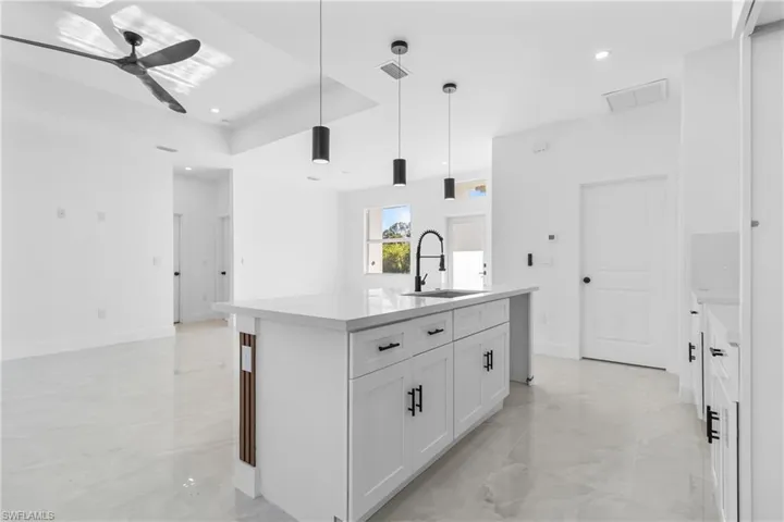 Kitchen featuring light stone counters, a kitchen island with sink, white cabinets, hanging light fixtures, and light marble finish floors