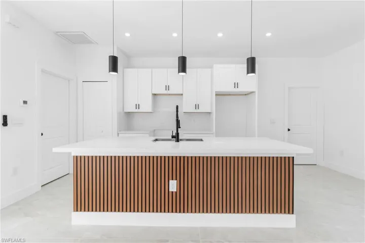 Kitchen featuring light stone counters, a large island with sink, white cabinets, decorative light fixtures, and a breakfast bar