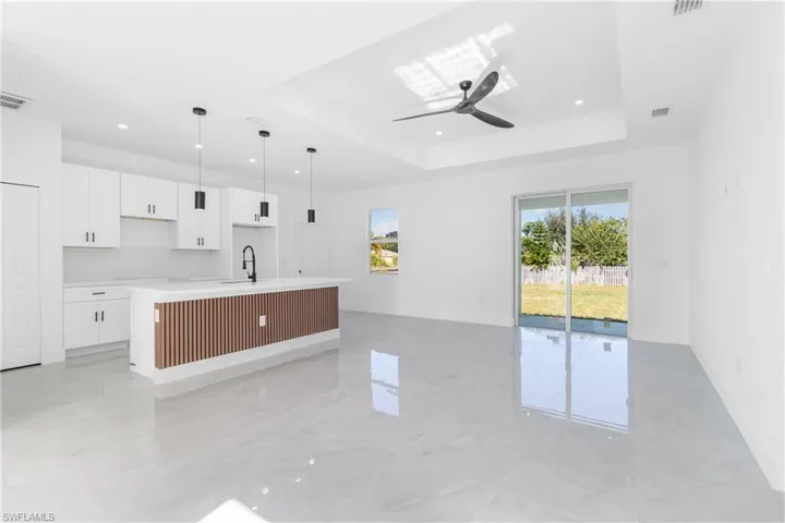 Kitchen featuring white cabinetry, an island with sink, decorative light fixtures, light stone countertops, and ceiling fan