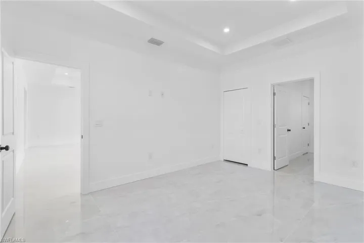 Unfurnished bedroom with a raised ceiling, recessed lighting, and ensuite bath
