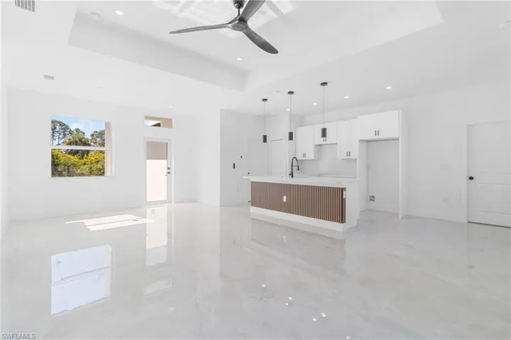 Unfurnished living room featuring a raised ceiling, a ceiling fan, and recessed lighting