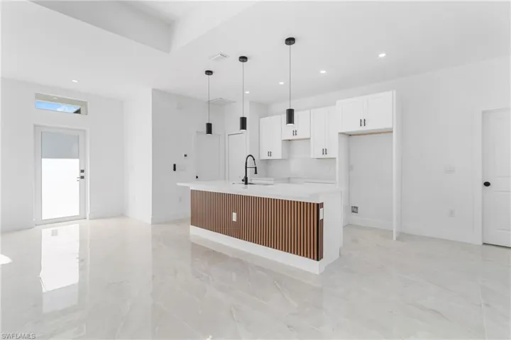 Kitchen featuring white cabinetry, pendant lighting, a kitchen island with sink, light stone countertops, and light marble finish floors