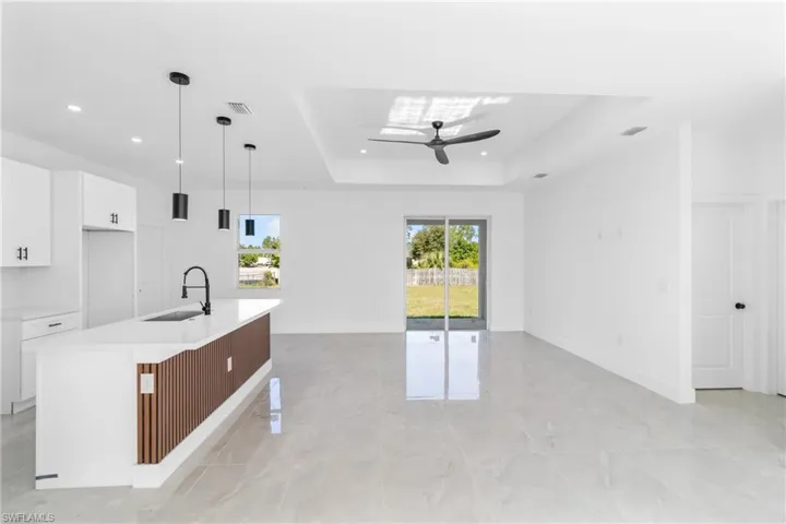 Kitchen with white cabinets, decorative light fixtures, a kitchen bar, a kitchen island with sink, and a tray ceiling
