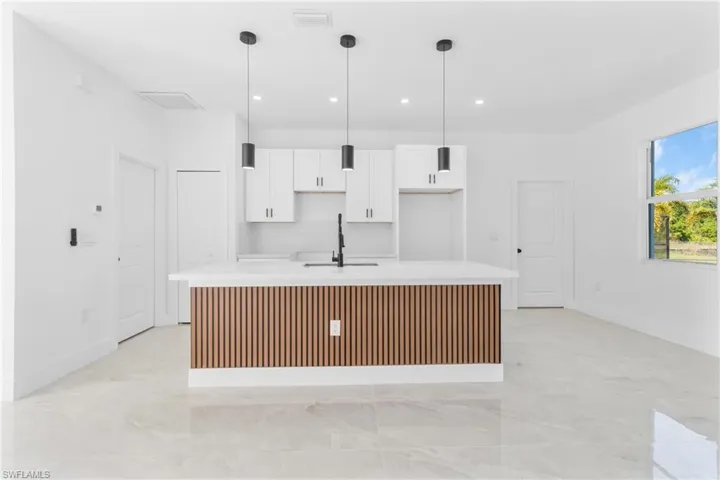 Kitchen featuring white cabinets, a kitchen island with sink, light stone counters, and decorative light fixtures