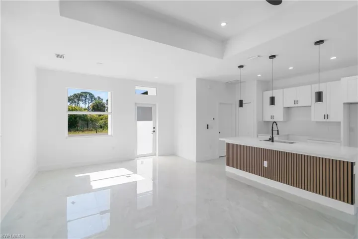 Kitchen featuring white cabinets, light stone counters, an island with sink, pendant lighting, and a tray ceiling