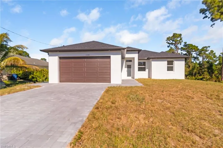 Prairie-style house featuring stucco siding, decorative driveway, an attached garage, and a front lawn