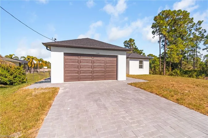View of front of home with a front lawn, stucco siding, a garage, and decorative driveway