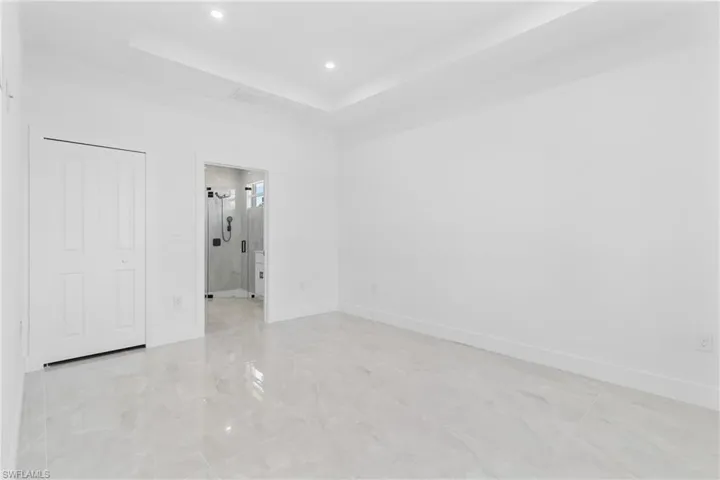 Unfurnished bedroom featuring a raised ceiling, recessed lighting, a closet, and ensuite bathroom