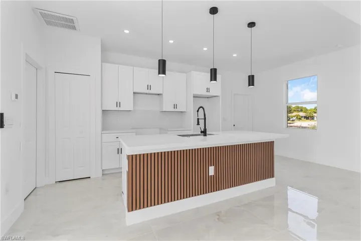 Kitchen featuring white cabinetry, a center island with sink, and decorative light fixtures
