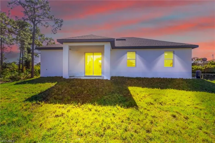 Back of property featuring stucco siding, a lawn, a patio area, and a shingled roof