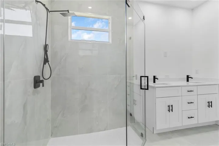 Full bath with double vanity and a marble finish shower