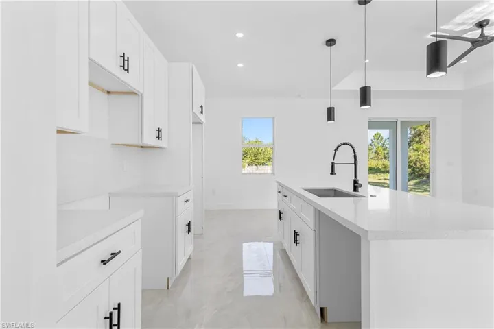 Kitchen featuring white cabinetry, light stone counters, decorative light fixtures, a center island with sink, and light marble finish floors