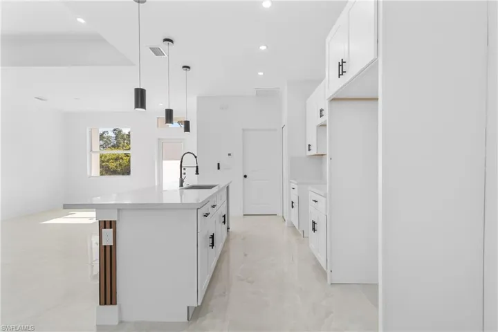 Kitchen featuring white cabinets, hanging light fixtures, light stone countertops, a breakfast bar area, and a kitchen island with sink