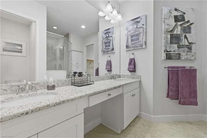 Full bathroom with a walk in closet, a shower stall, double vanity, and light tile patterned floors
