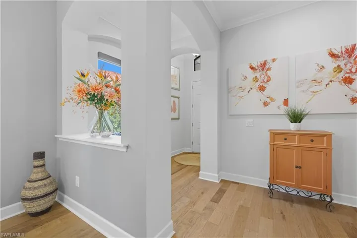 Hallway with crown molding, light wood-type flooring, and arched walkways