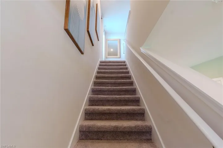 Carpeted staircase with white handrail and trim, leading to an upper level with light-colored walls
