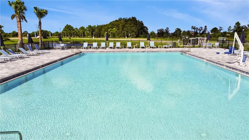 Expansive outdoor swimming pool featuring a light-colored finish, surrounding paver decking, multiple lounge chairs, and mature palm trees