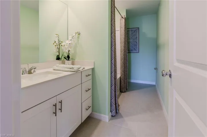 Bathroom with a single basin vanity featuring white cabinetry and light-toned countertop, a large wall mirror, and light green walls