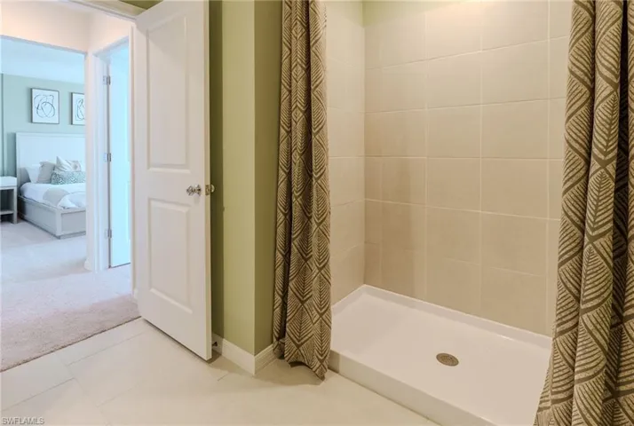 Shower enclosure featuring light-toned tile walls and a white shower base
