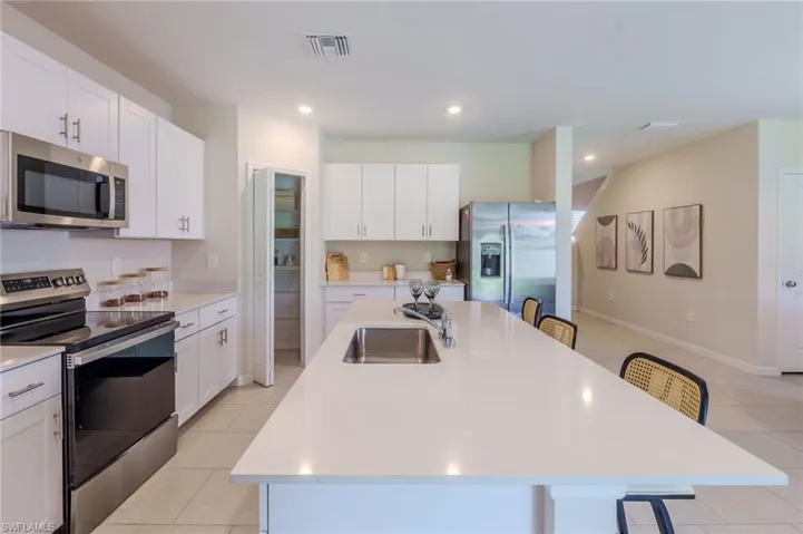Open-concept kitchen featuring white cabinetry, stainless steel appliances, a large center island with an undermount sink, and light-toned tile flooring