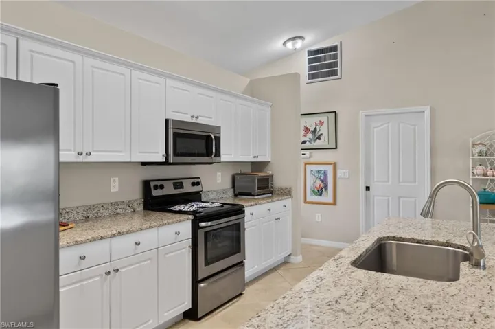 Kitchen with white cabinets, appliances with stainless steel finishes, light stone counters, sink, and lofted ceiling