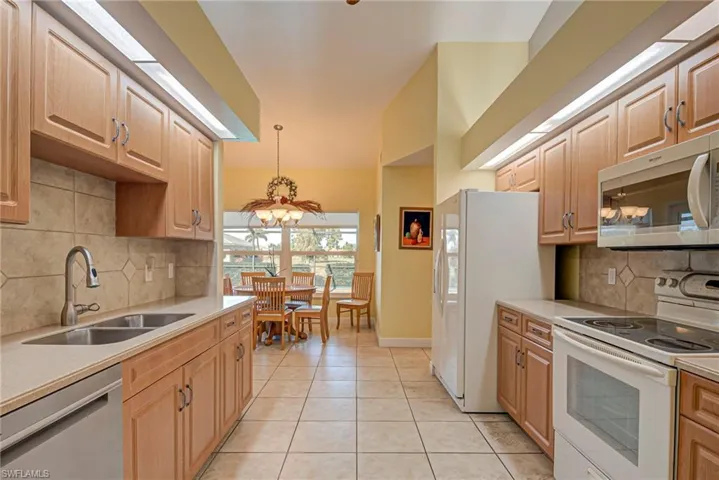 Kitchen featuring decorative backsplash, white appliances, light wood finish cabinetry, and light tile patterned floors