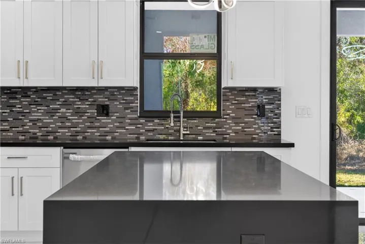 Kitchen featuring white cabinetry, stainless steel dishwasher, plenty of natural light, and dark stone countertops