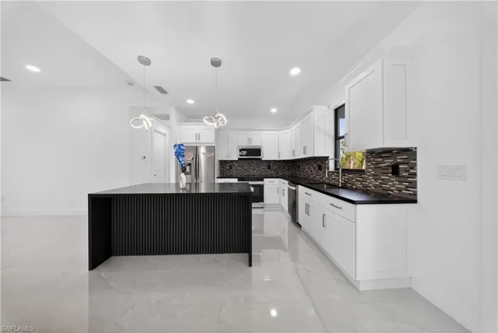 Kitchen with a kitchen island, white cabinetry, decorative light fixtures, and stainless steel appliances