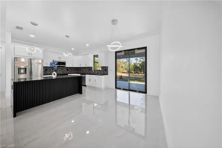 Kitchen with a kitchen island, white cabinets, pendant lighting, stainless steel appliances, and decorative backsplash
