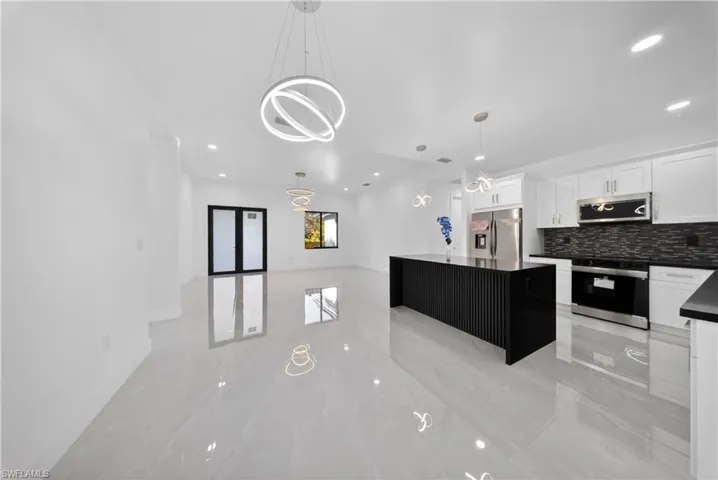 Kitchen featuring a kitchen island, dark cabinets, stainless steel appliances, decorative light fixtures, and light marble finish floors