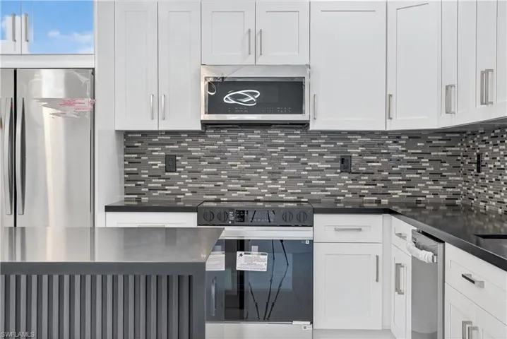 Kitchen with stainless steel appliances, white cabinetry, and backsplash