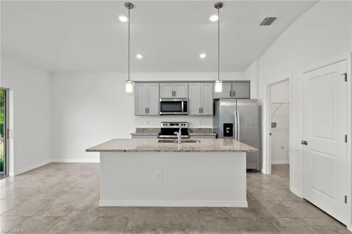 Kitchen featuring stainless steel appliances, light tile flooring, a center island with sink, and pendant lighting