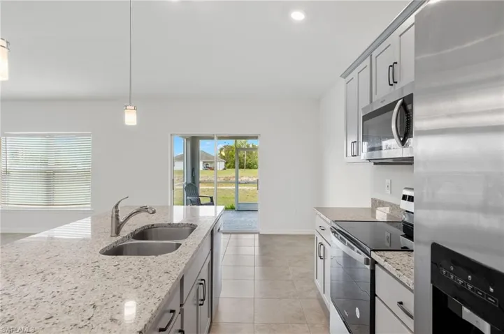 Kitchen with light stone counters, hanging light fixtures, appliances with stainless steel finishes, sink, and light tile floors